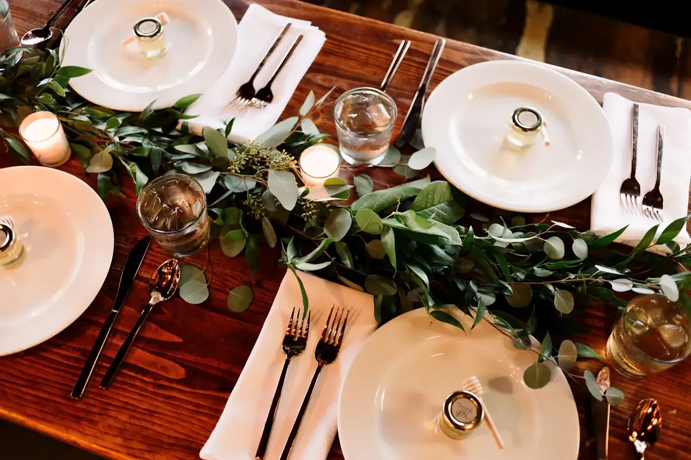 Long wooden banquet table dressed with a trailing eucalyptus garland and scattered candles