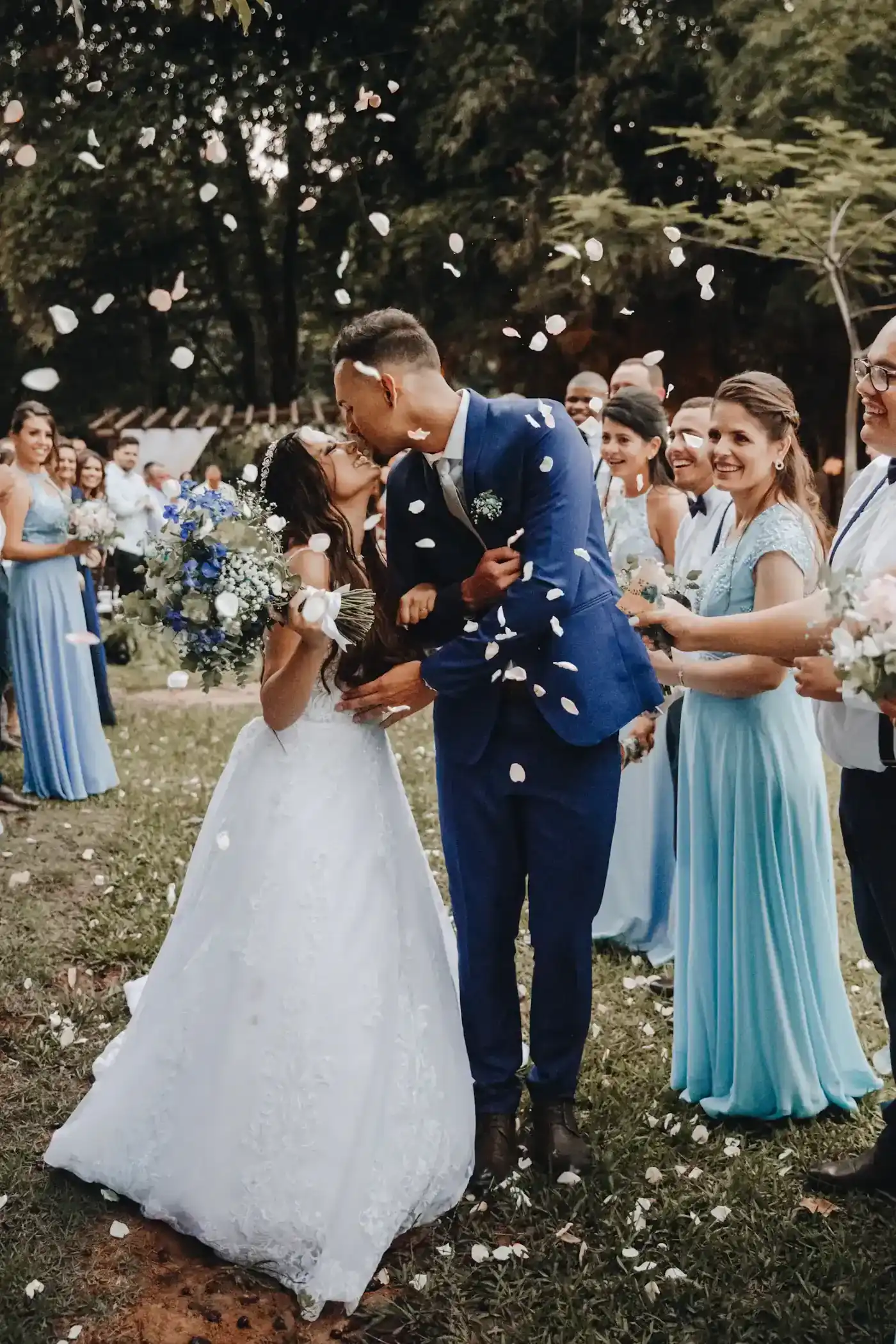 Newlyweds kissing as joyful wedding guests shower them with flower petals at an outdoor celebration