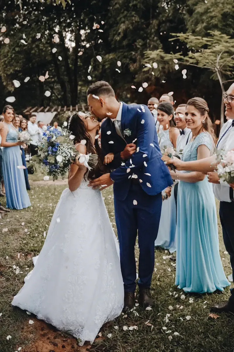 Newlyweds kissing as wedding guests shower them with flower petals at a joyful outdoor celebration